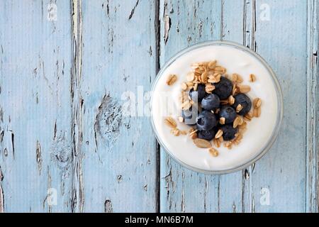 Griechischer Joghurt mit Heidelbeeren und Müsli, Blick nach unten auf einem urigen Soft blau Holz Hintergrund Stockfoto