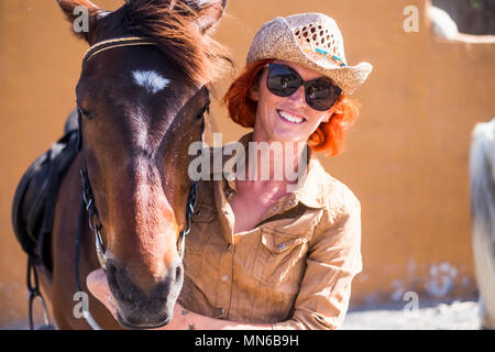 Lächelte schöne Mädchen, rotes Haar und Cowboy Hut mit Ihrem besten Freund Pferd in Freundschaft bereit, ein weiteres Abenteuer im Freien und in der Freizeit zu leben Stockfoto