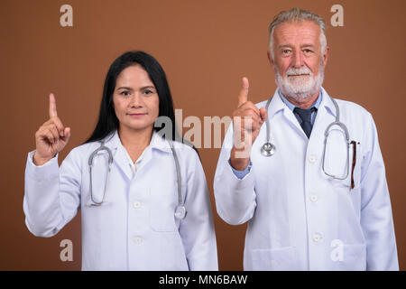 Ausgereifte multi-ethnischen paar Ärzte gegen braunen Hintergrund Stockfoto