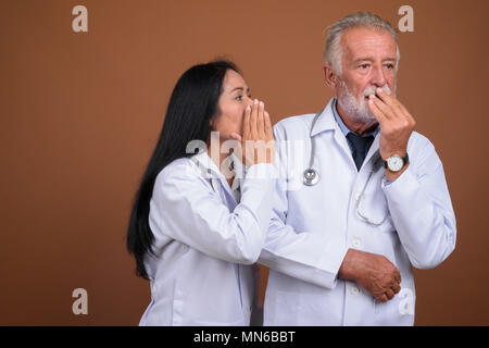 Ausgereifte multi-ethnischen paar Ärzte gegen braunen Hintergrund Stockfoto