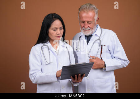 Ausgereifte multi-ethnischen paar Ärzte gegen braunen Hintergrund Stockfoto