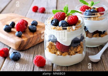 Heidelbeere und Himbeere parfaits in Mason jars, Szene auf einem rustikalen, mit Holz Hintergrund Stockfoto