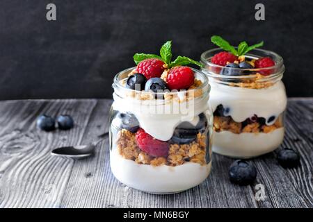 Gesunde Heidelbeere und Himbeere parfaits in Mason jars, Szene auf dunklen rustikalen Hintergrund Stockfoto