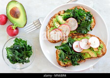 Avocado Toast mit Kohl und Rettich auf Vollkornbrot, Overhead Szene auf Marmor Stockfoto