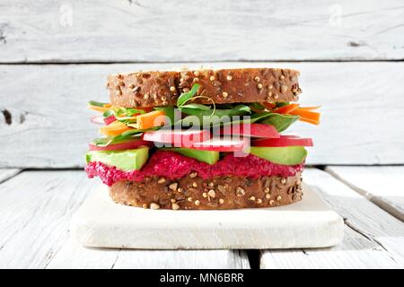 Superfood Sandwich mit Zuckerrüben Hummus, Avocado, Gemüse und Grüns, auf Vollkornbrot gegen einen weißen Holz Hintergrund Stockfoto