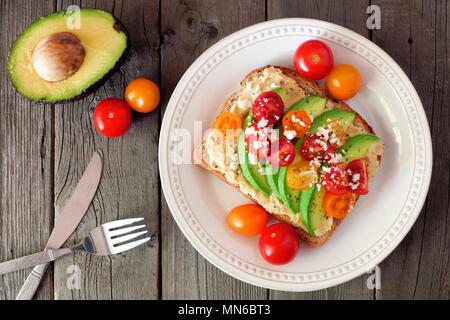 Avocado Toast mit Hummus und Tomaten auf Platte, oben Szene auf alten Holz Hintergrund Stockfoto