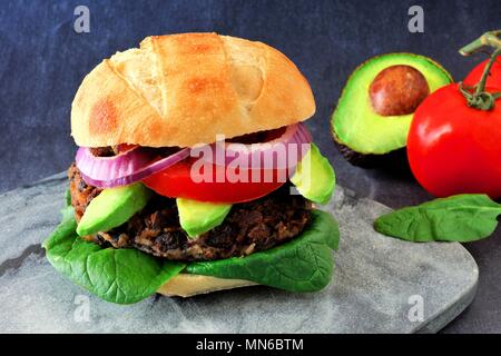 Veggie Bean und Süßkartoffel Burger mit Avocado und Spinat vor einem dunklen Hintergrund Stockfoto