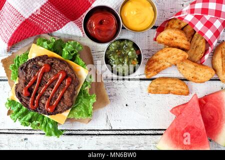 Picknick Szene mit offenen Hamburger, Wassermelone und Potato Wedges auf weißem Holz Hintergrund Stockfoto