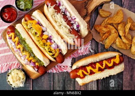 Hot dogs mit verschiedenen Toppings und Kartoffelecken, oben Blick auf eine rustikale Holz Hintergrund Stockfoto