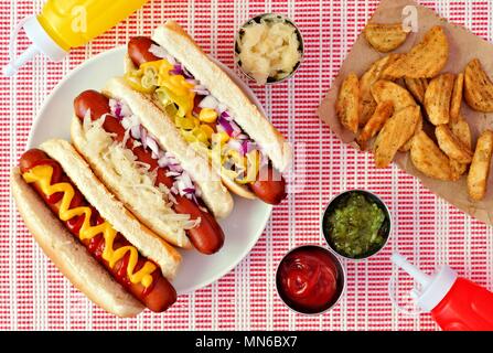 Hot dogs mit verschiedenen Toppings und Kartoffelecken, oben Szene auf einem roten und einem weißen Tuch Stockfoto