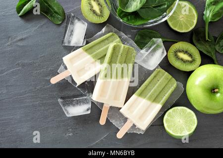 Fraktion der Grünen smoothie Eis am Stiel mit Kiwi, Spinat, Apple und Limetten, oben Blick auf dunklem Schiefer Hintergrund Stockfoto