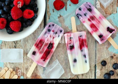 Gruppe von hausgemachten Mixed berry Joghurt Eis am Stiel auf eine rustikale Holz Hintergrund Stockfoto