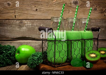Grüne Smoothies in Milchflaschen in einem vintage Drahtkorb gegen eine rustikale Holz Hintergrund Stockfoto