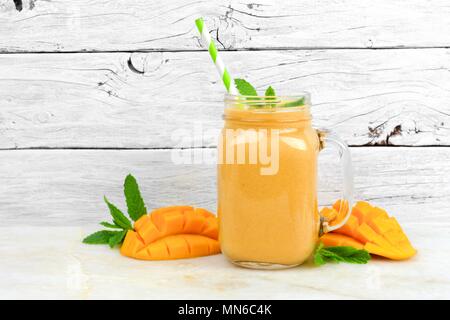 Tropische mango coconut Smoothie in einem Marmeladenglas Glas, auf einem urigen weiß Holz Hintergrund Stockfoto