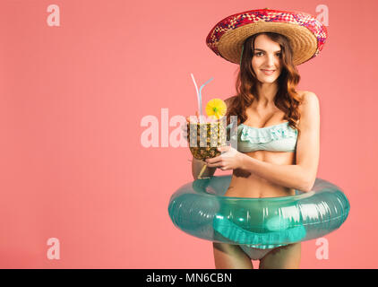 Junge Frau in Bikini und Sombrero mit Schwimmring, tropischen Cocktail auf rosa Hintergrund, kopieren Platz Stockfoto