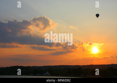 Ein Ballon fliegen über den Himmel, während die Sonne hinter dem golden Wolken geht. Stockfoto