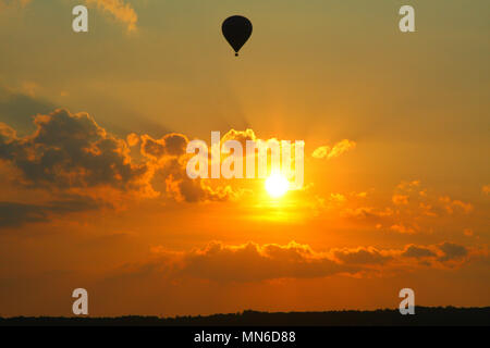 Ein Ballon fliegen über den Himmel, während die Sonne hinter dem golden Wolken geht. Stockfoto