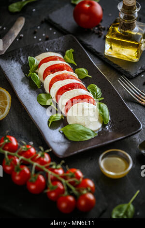 Traditionelle italienische Tomatensalat caprese mit Mozzarella und Basilikum auf einer schwarzen Platte Stockfoto