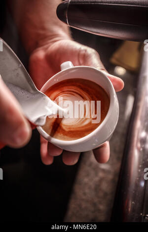 Barista macht Kaffee latte Kunst, er gießt Milch Stockfoto