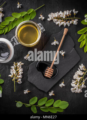 Krug Honig mit Blumen von Akazienholz auf schwarzem Hintergrund Stockfoto