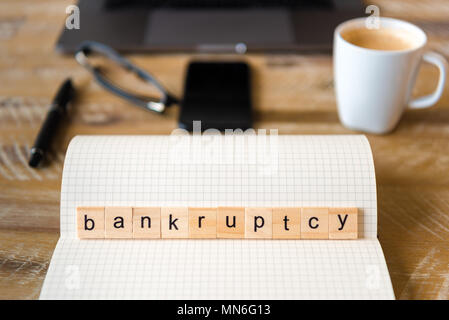 Nahaufnahme auf das Notebook um Holz Tisch Hintergrund, auf Holzblöcken mit Buchstaben machen Bankrott Wort konzentrieren. Business Concept Bild. Laptop, Gläser, p Stockfoto