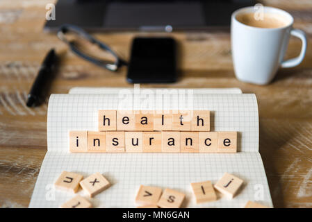 Nahaufnahme auf das Notebook um Holz Tisch Hintergrund, auf Holzblöcken mit Buchstaben, Krankenversicherung Worte konzentrieren. Stockfoto