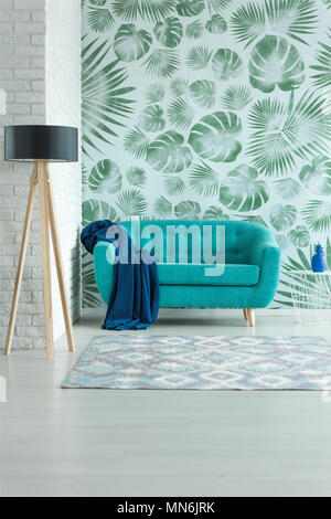 Holz- Lampe und blaue Decke auf Aquamarin Sofa im hellen Wohnzimmer mit Blättern wallpaper Stockfoto