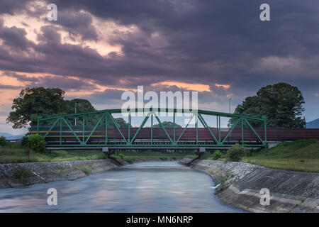 Motion Blur lange Belichtung Zug passiert über metallische Eisenbahnbrücke während der Blauen Stunde mit Sky noch dramatische nach Sonnenuntergang Stockfoto