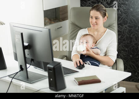 Porträt der jungen Selbständigen Frau, die zu Hause arbeiten und die Milch für Ihr Baby Sohn Stockfoto