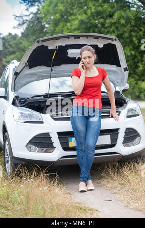 Junge Frau lehnte sich auf gebrochene Auto mit offener Haube und Assistance Service Stockfoto