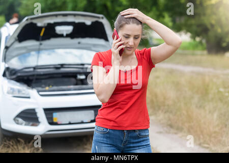 Verärgert betonte Frau im Gespräch mit Auto Service per Handy auf der Landstraße Stockfoto
