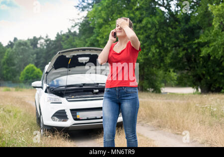 Betonte junge Frau mit kaputten Auto auf Landstraße Aufruf car service Stockfoto