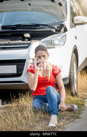 Junge Frau sitzt auf dem Boden neben dem kaputten Auto, Auto Service für Hilfe umgekippt Stockfoto