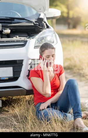 Junge Frau in Ihr defektes Auto im Feld sitzen und Abschleppwagen rufen um Hilfe umgekippt Stockfoto