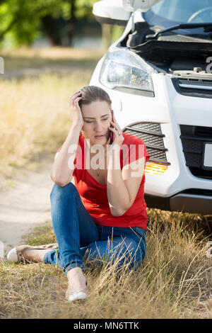 Junge weinende Frau an Ihr defektes Auto im Feld sitzen und Aufruf von Auto Service Stockfoto