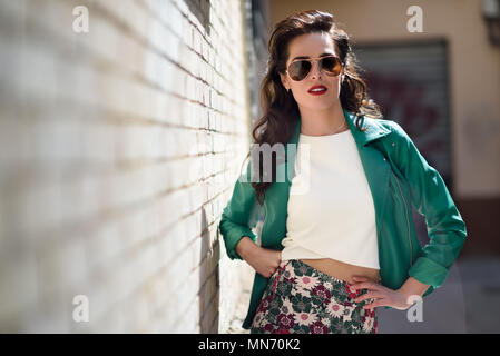 Junge brünette Frau mit Aviator Sonnenbrille. Mädchen, Modell der Mode, das Tragen von grünen moderne Jacke, im städtischen Hintergrund stehen. Stockfoto