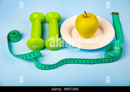 Apple auf der Platte, Hanteln und Maßband auf einem blauen Hintergrund aus Holz. Konzept der Ernährung und gesunde Lebensweise. Stockfoto