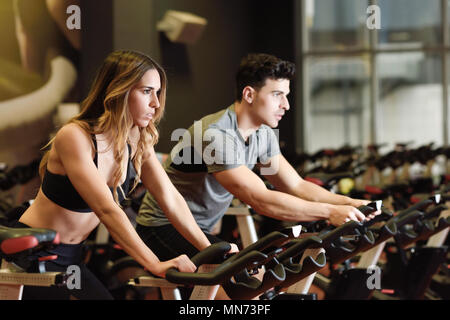 Zwei Menschen biken im Fitnessraum trainieren Beine tun cardio Workout radfahren Fahrräder. Paar in einer Spinnerei klasse Sportkleidung zu tragen. Stockfoto