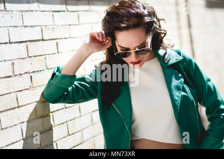 Junge brünette Frau mit Aviator Sonnenbrille. Mädchen, Modell der Mode, das Tragen von grünen moderne Jacke, im städtischen Hintergrund stehen. Stockfoto