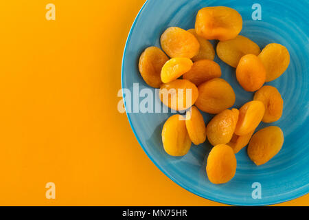 Ganze getrocknete Aprikosen Obst auf der cyanfarbenen Platte auf dem orangen Hintergrund von oben Stockfoto