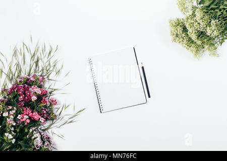 Tagebuch öffnen Sie das Blatt unter Rosa und grün Blumen auf weißem Hintergrund, Ansicht von oben. Feminine flach Mock-up von leeren Notizblock und Bleistift. Stockfoto