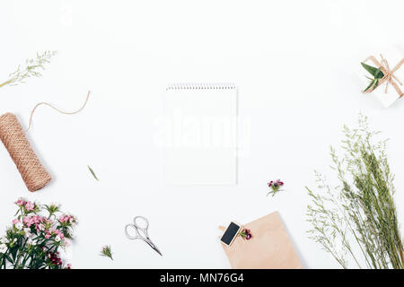 Leere notepad Blatt von Blumen, Garn, grün Ährchen und Geschenke auf weißem Hintergrund, Ansicht von oben umgeben. Flach Zusammensetzung leer Tagebuch in der cen Stockfoto