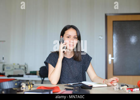Junge Frau sitzend an Leder Atelier und handmade Notebook und Mappen, Reden von Smartphone Stockfoto