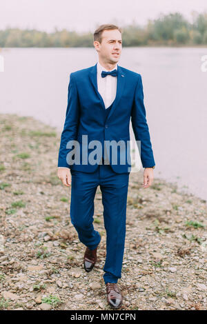 In voller Länge Foto der Bräutigam zur Seite während der Wanderung am Strand entlang. Stockfoto