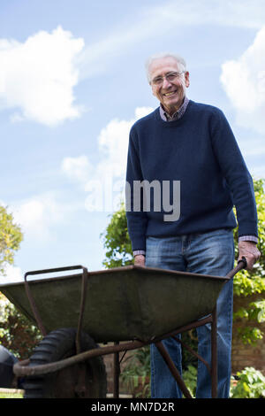 Portrait von älteren Mann drücken Barrow während der Gartenarbeit Stockfoto