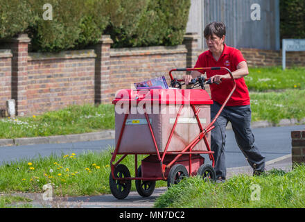Frau treibt ein Royal Mail Warenkorb bei gleichzeitiger Bereitstellung von Buchstaben und Post in England, Großbritannien. Stockfoto