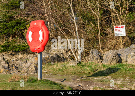 Ein lebensrettender Ring oder Rettungsschwimmer und ein Gefahrenschild an der Küstenlinie der renownedly verräterischen Morecambe Bay. Arnside, Großbritannien. April 2018. Stockfoto