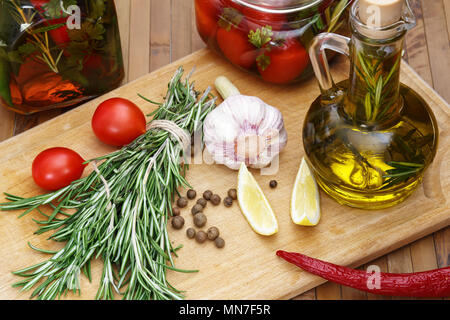 Home Canning. Rosmarin, Piment, Chili, Knoblauch, Zitrone, Olivenöl, Tomaten, Gläser Essiggurken auf dem Küchentisch. Stockfoto