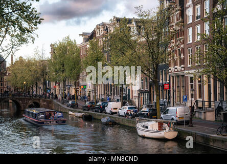 Amsterdam, Niederlande - 27 April 2017: Hausboote und Binnenschiffe, die Binnenamstel canal gegen typische holländische Häuser mit Flagge der Niederlande und Stockfoto