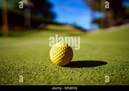 Minigolf gelbe Kugel auf grünem Gras bei Sonnenuntergang Stockfoto